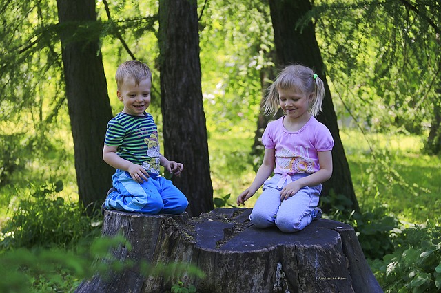 děti v lese, kluk a holka sedí na pařezu